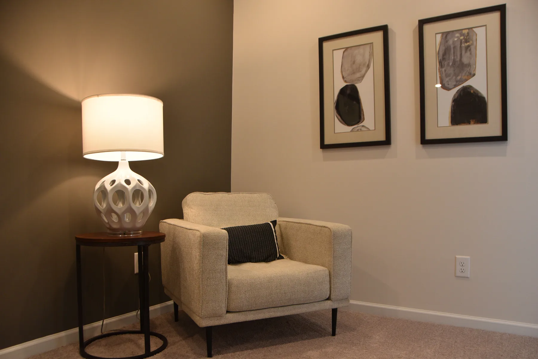Corner of a finished drawing room with an armchair, table lamp and framed prints